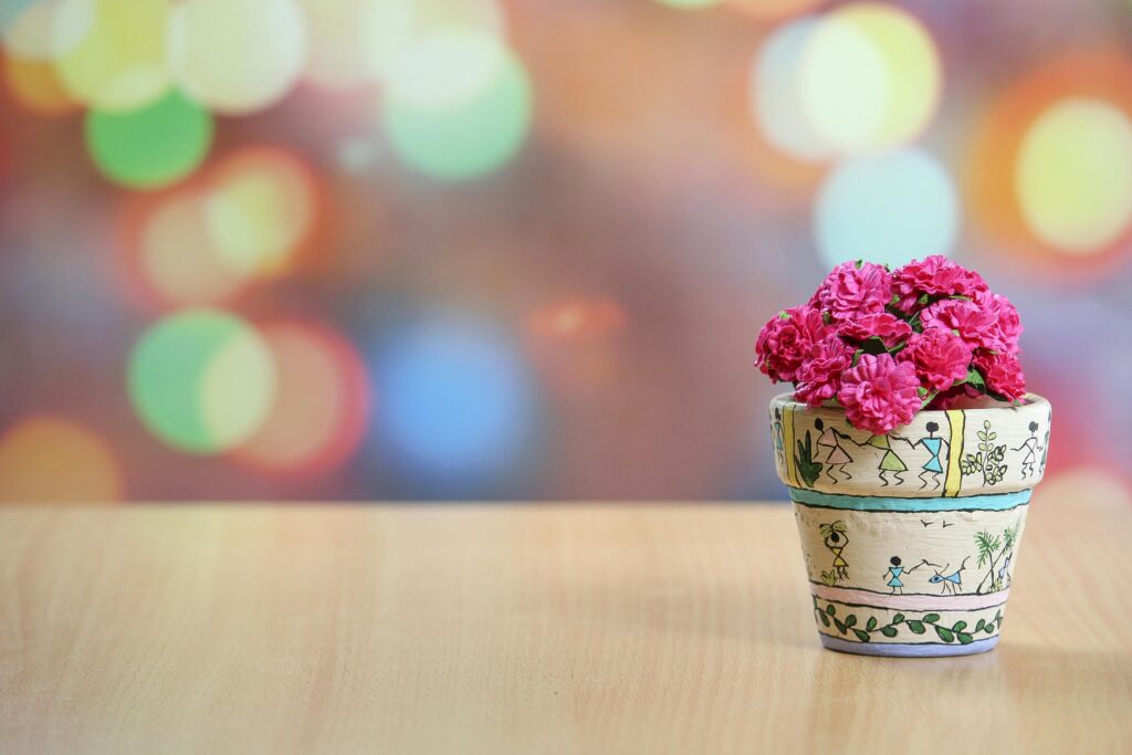 Vibrant pink flowers in a decorative pot against a colorful bokeh backdrop.